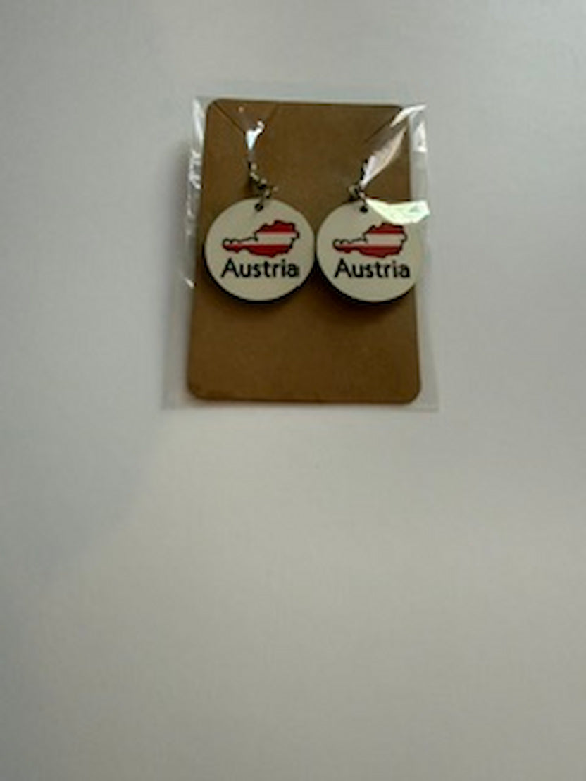 Austria map earrings attached to a brown backing card inside a clear plastic sleeve, showing red and white map designs with “Austria” text printed below. Roxzell