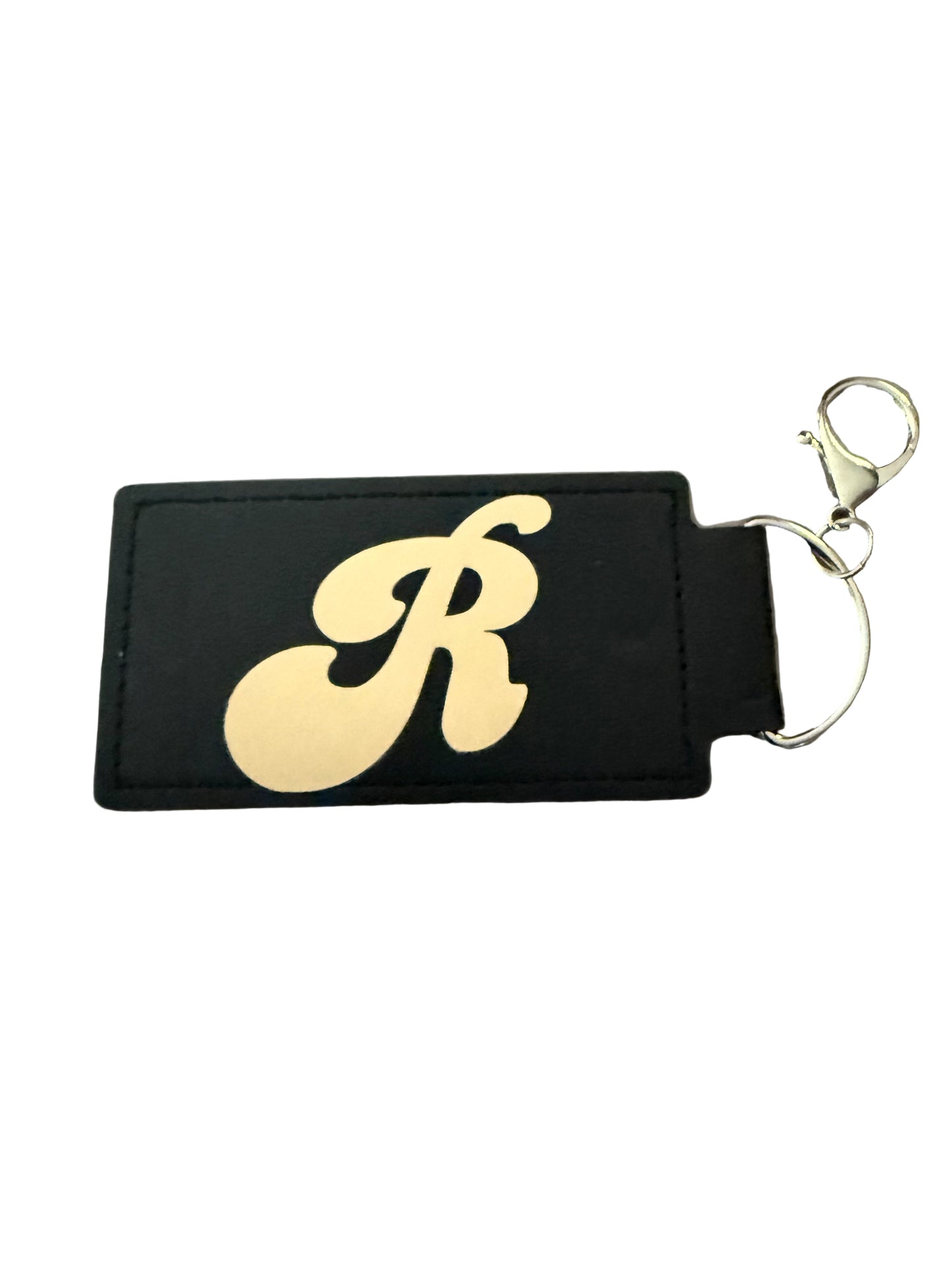 A black faux leather keychain with gold book and floral design, and a gold 'R' initial on reverse side, silver d-ring clasp Roxzell