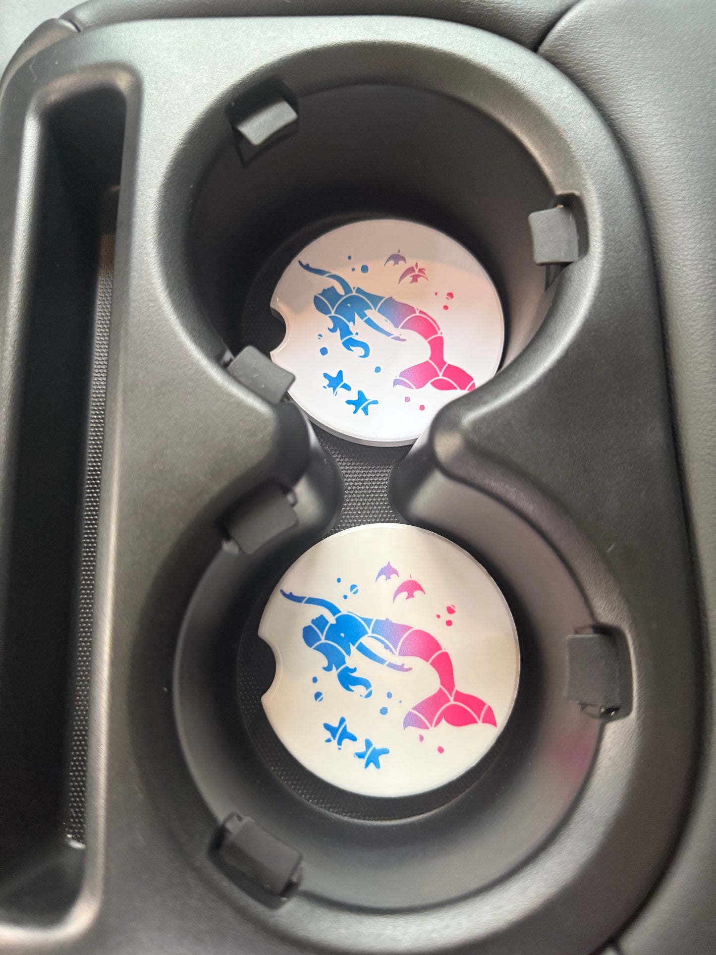 Two car cup holders with decorative car coasters featuring blue and pink mermaids.