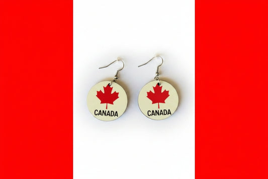 Pair of circular earrings featuring red maple leaves and the word “Canada” printed in black on a white background, displayed on a red and white surface.