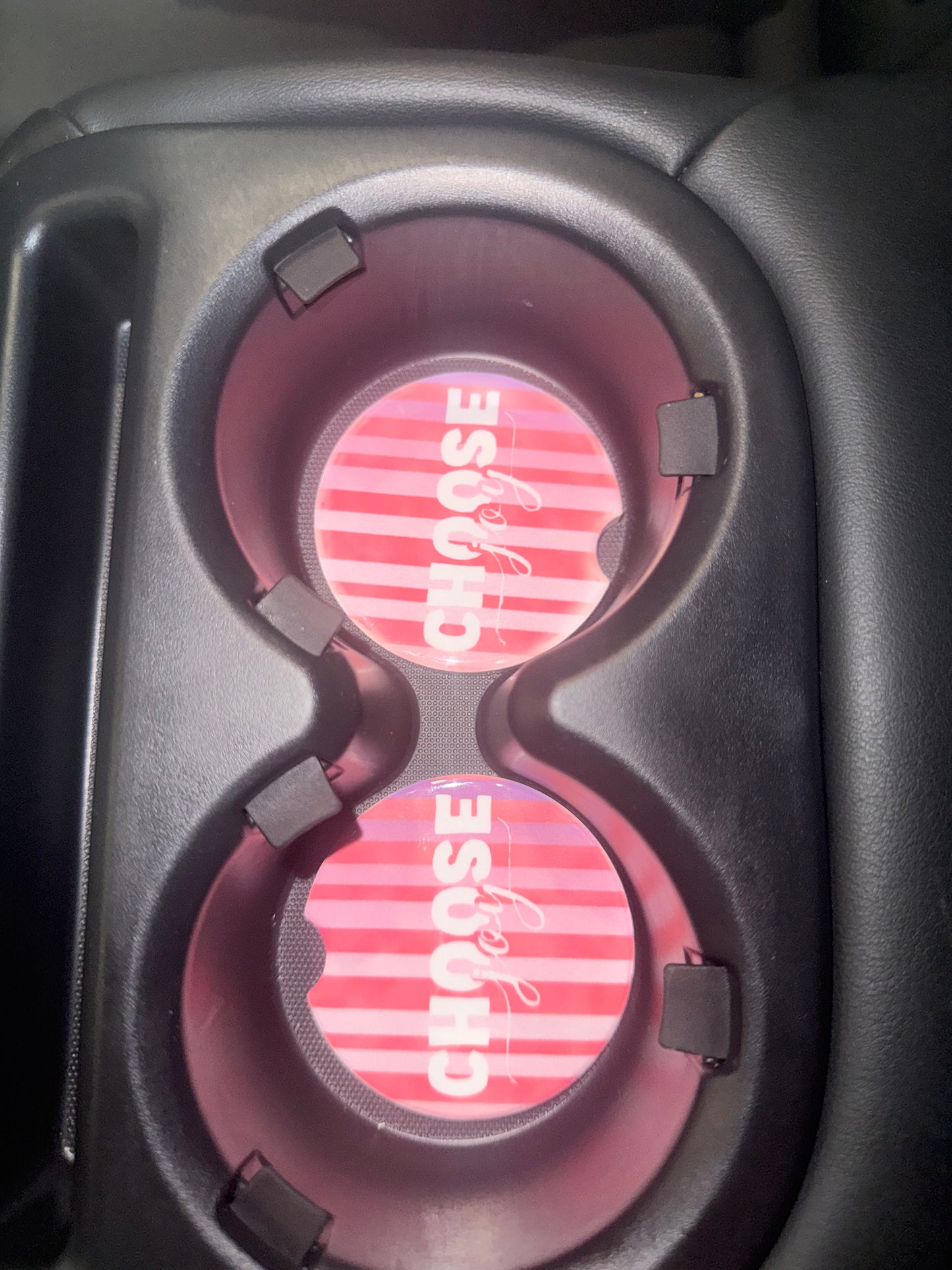 Two pink striped coasters with "Choose Joy" text in a car cup holder.