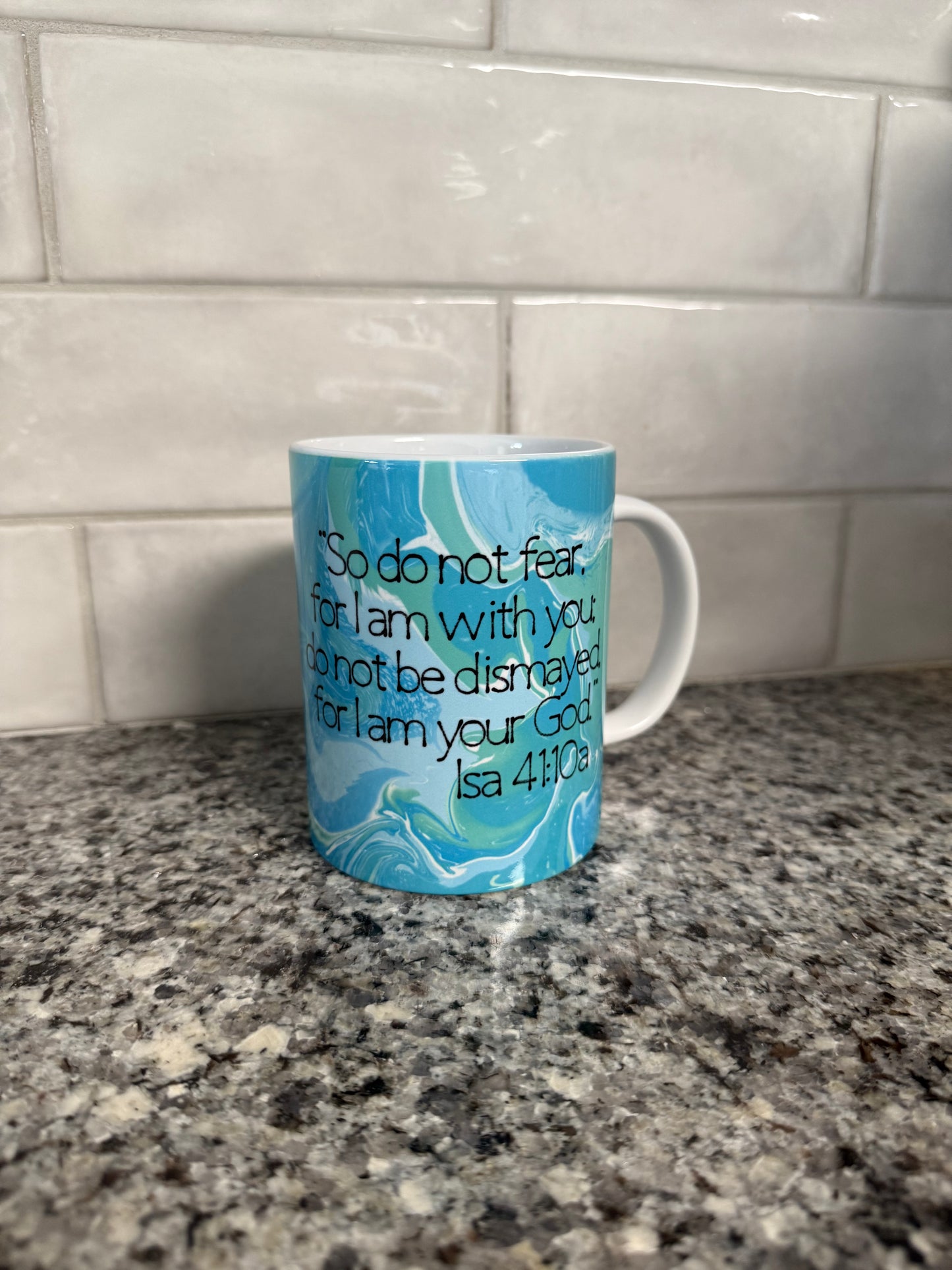 A ceramic coffee mug with a blue and white color scheme featuring scripture Isa 41:10a "So do no fear.... Roxzell