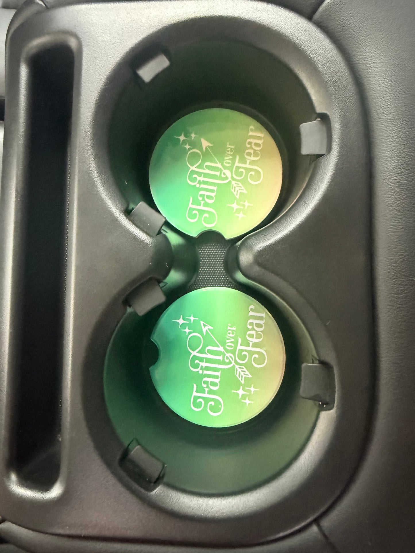 Two green car coasters with text "Faith over Fear" in a cup holder of a vehicle.