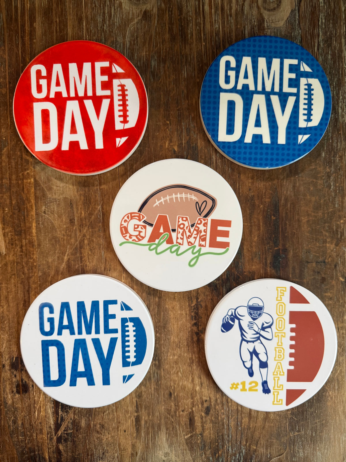 Group of five round football‑themed coasters featuring “GAME DAY” and “FOOTBALL” designs in red, blue, brown, and white tones. Roxzell