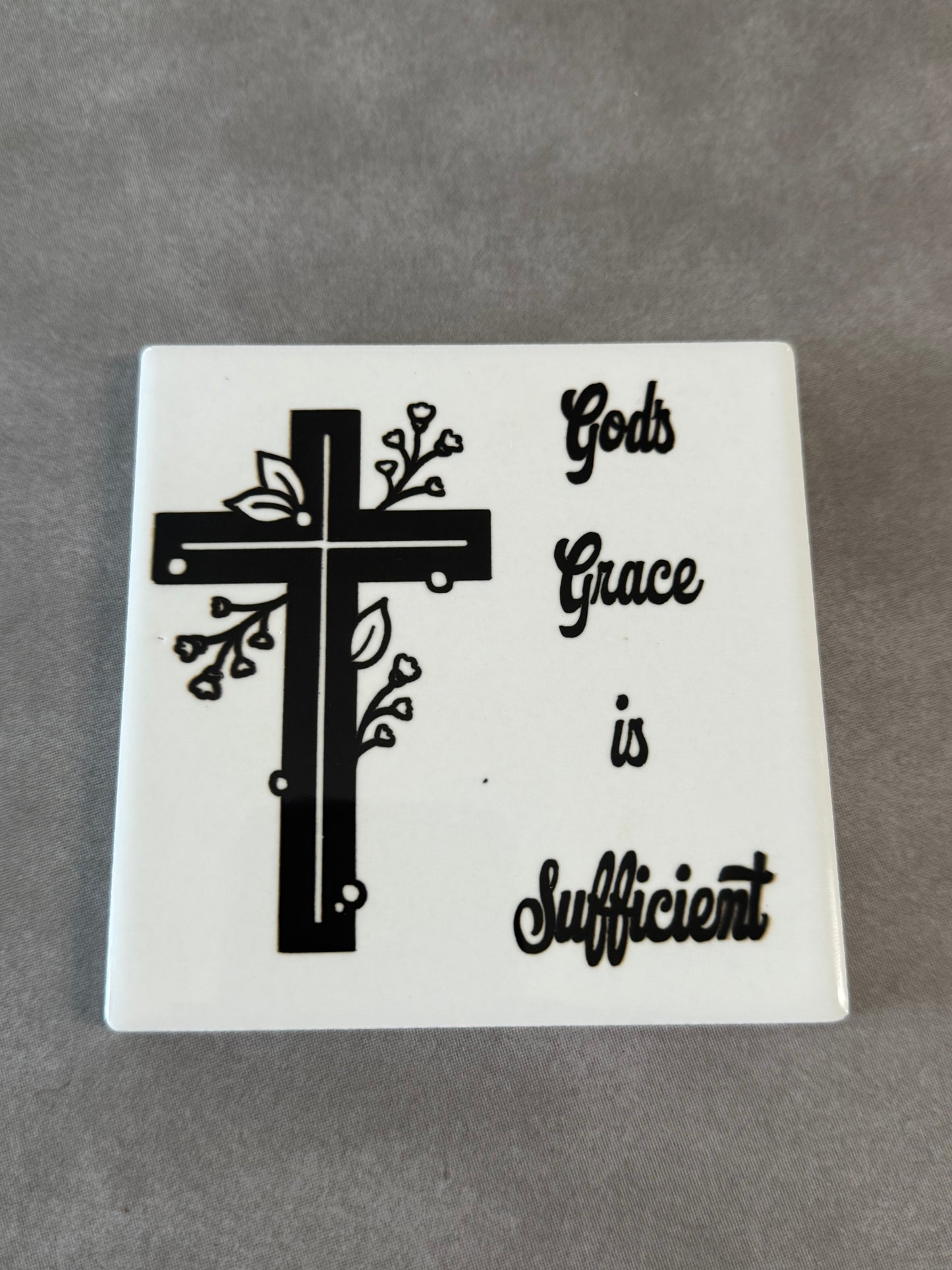 Square white ceramic coaster with black and white cross and words "God's Grace is Sufficient".