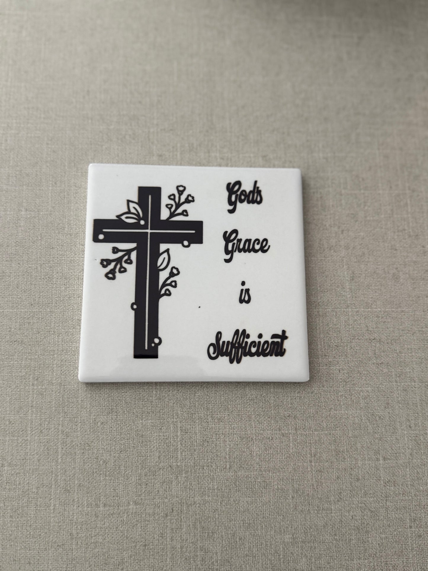 Square white ceramic coaster with black and white cross and words "God's Grace is Sufficient".