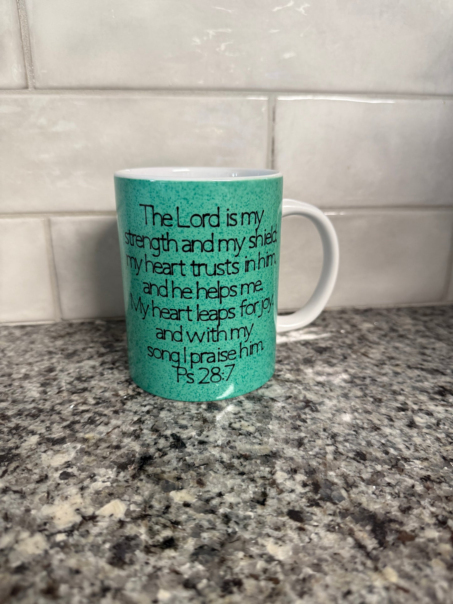 A green ceramic coffee/tea mug with the word 'JOY' written on it, displayed against a kitchen backdrop.