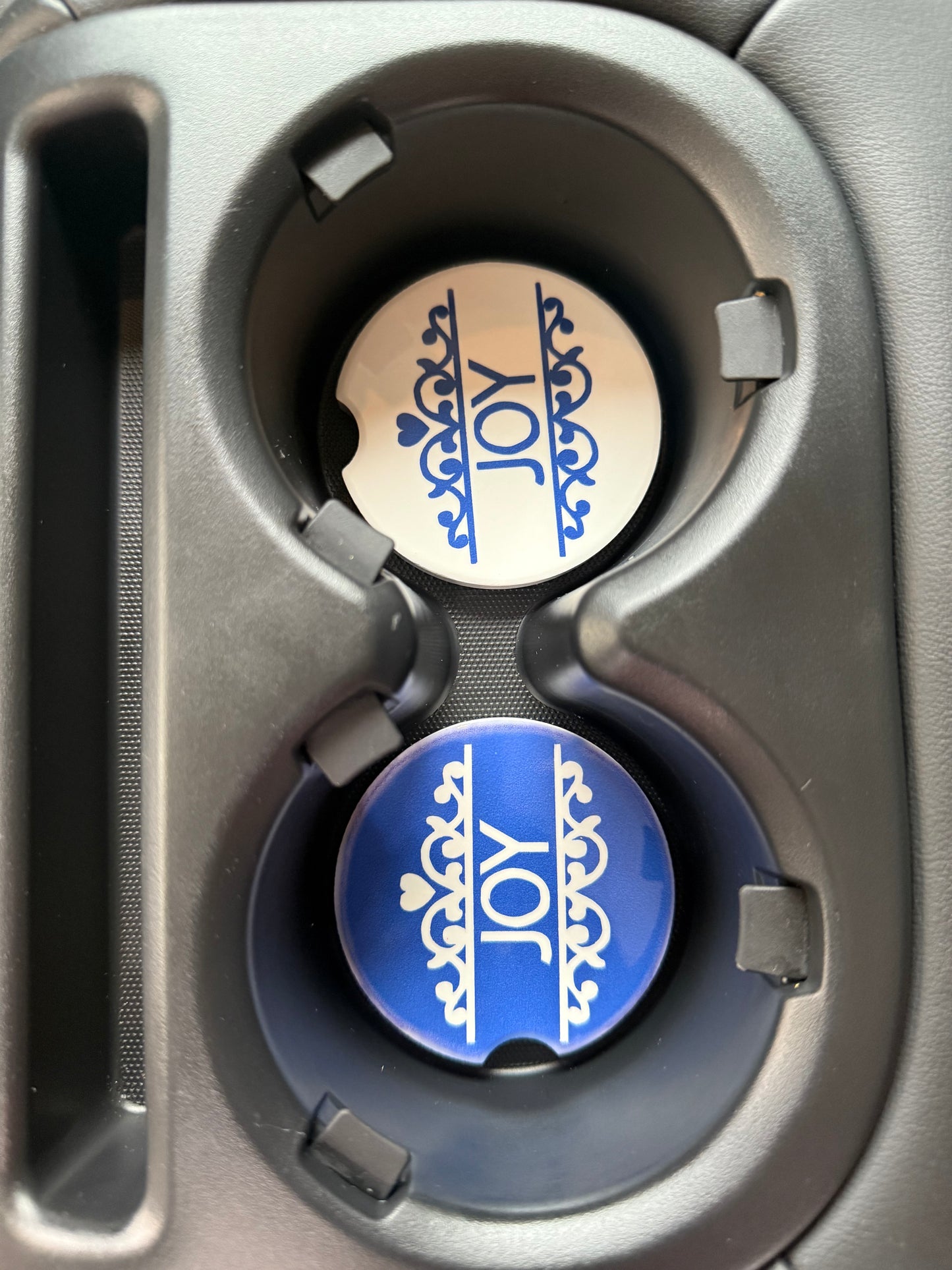 Two car coasters with 'JOY' design in a cup holder.