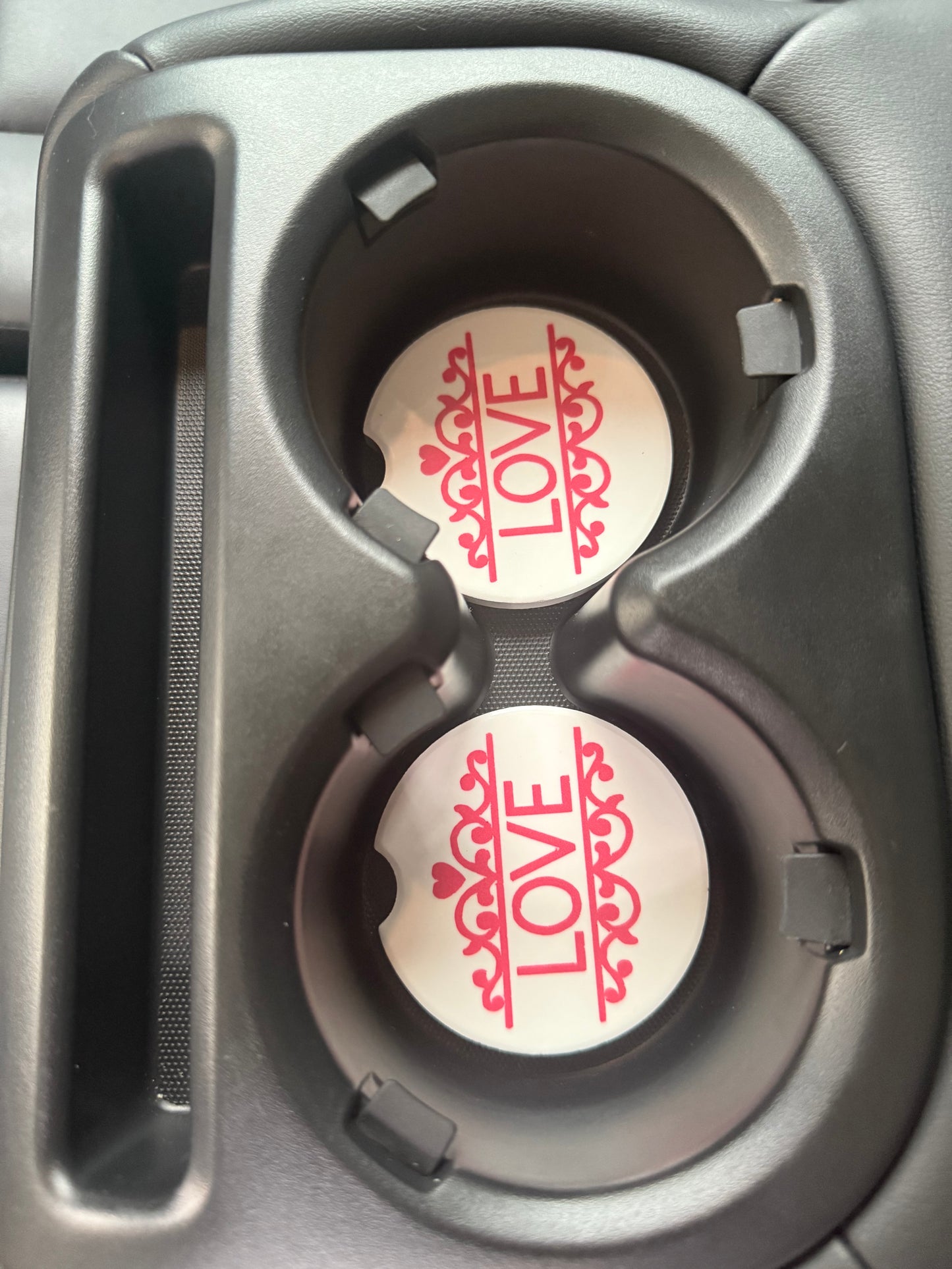 Two cup holders in a car with 'LOVE' and decorative designs.