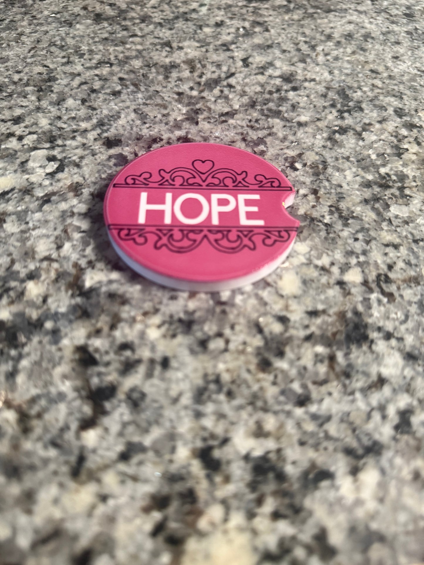 Pink 'HOPE' car coaster on a textured stone surface