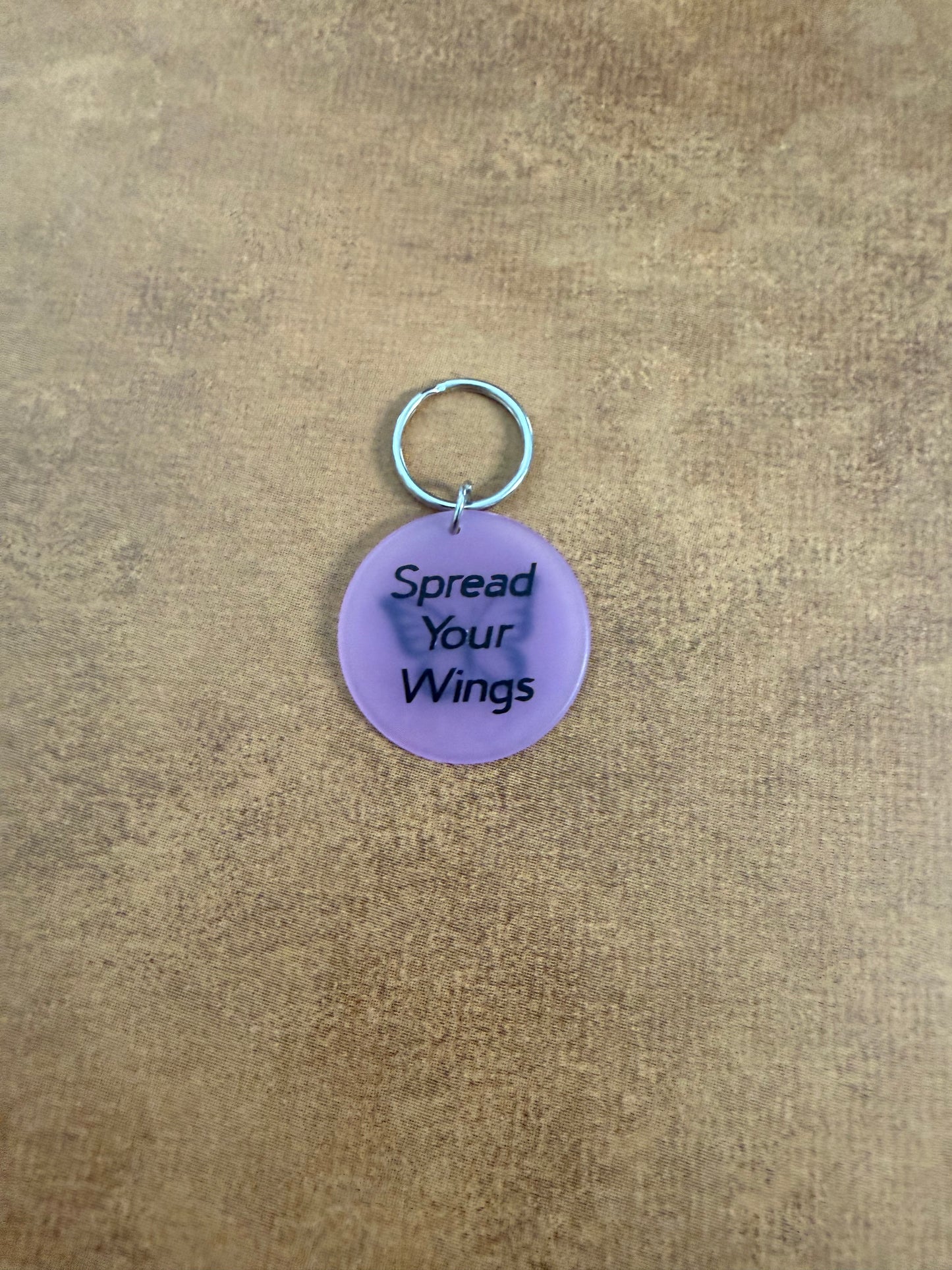 Purple acrylic butterfly keychain with "Spread Your Wings" on the reverse side.