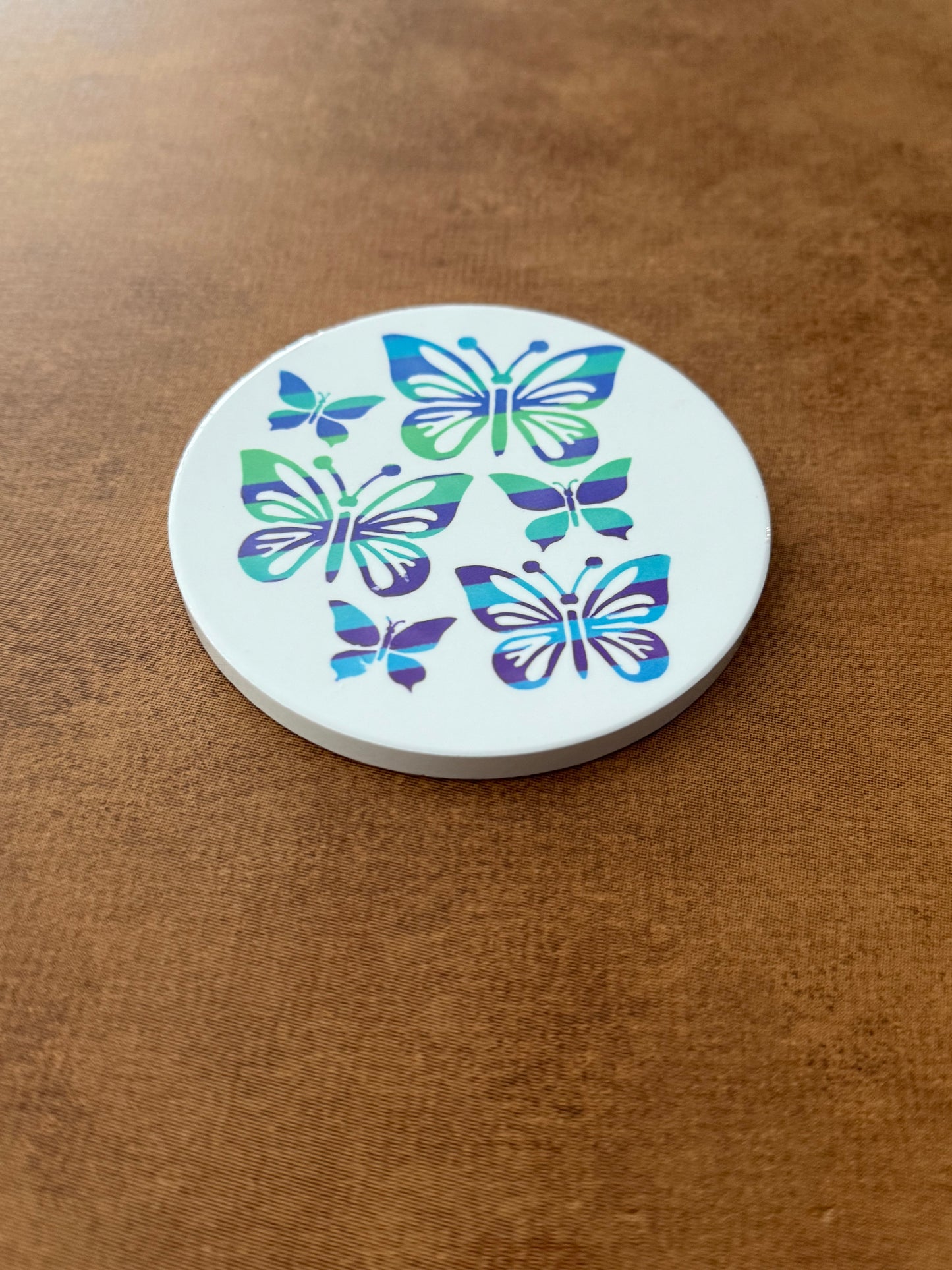 Round ceramic white coaster designed with blue and green butterflies.