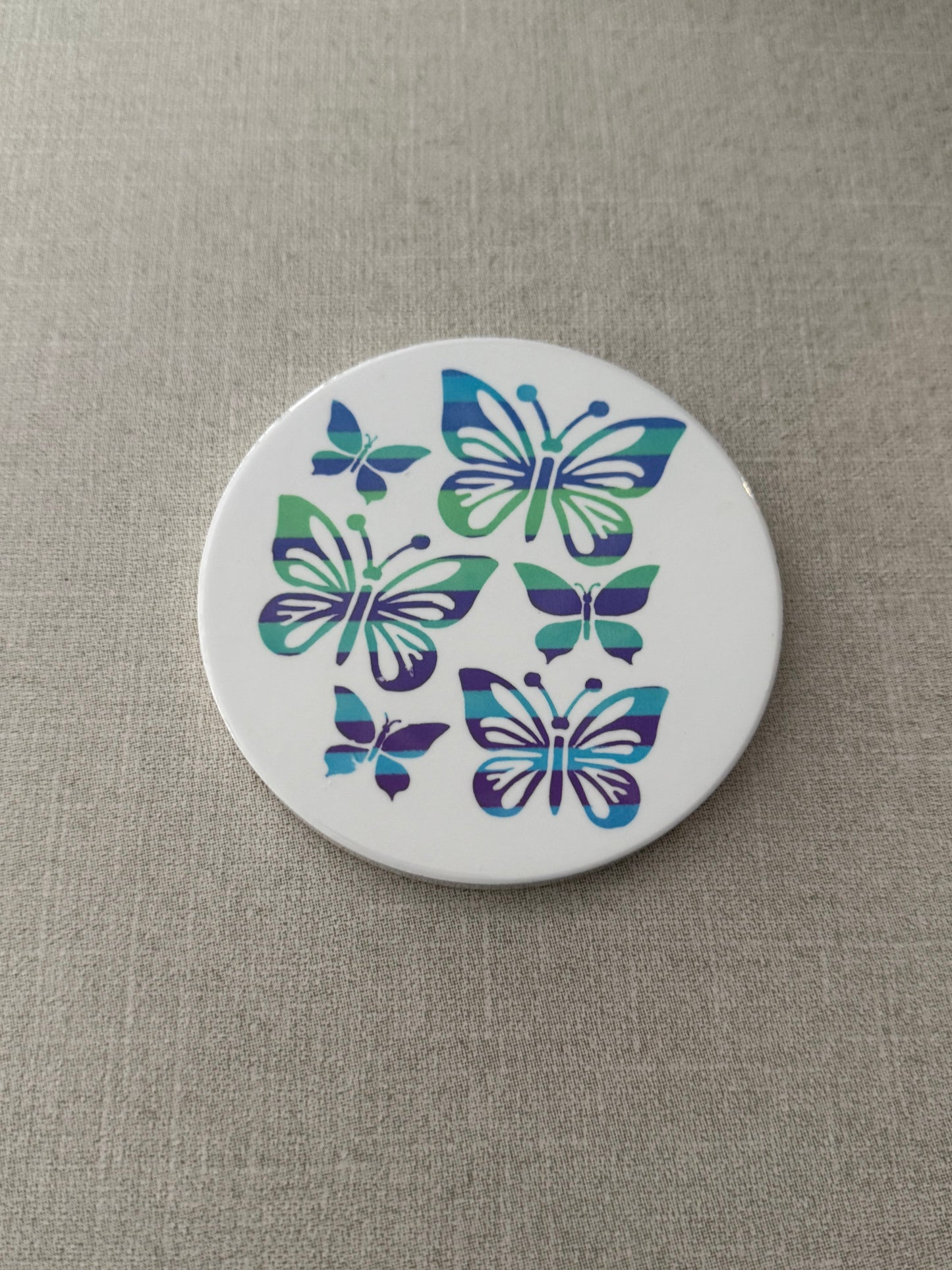 Round ceramic white coaster designed with blue and green butterflies.