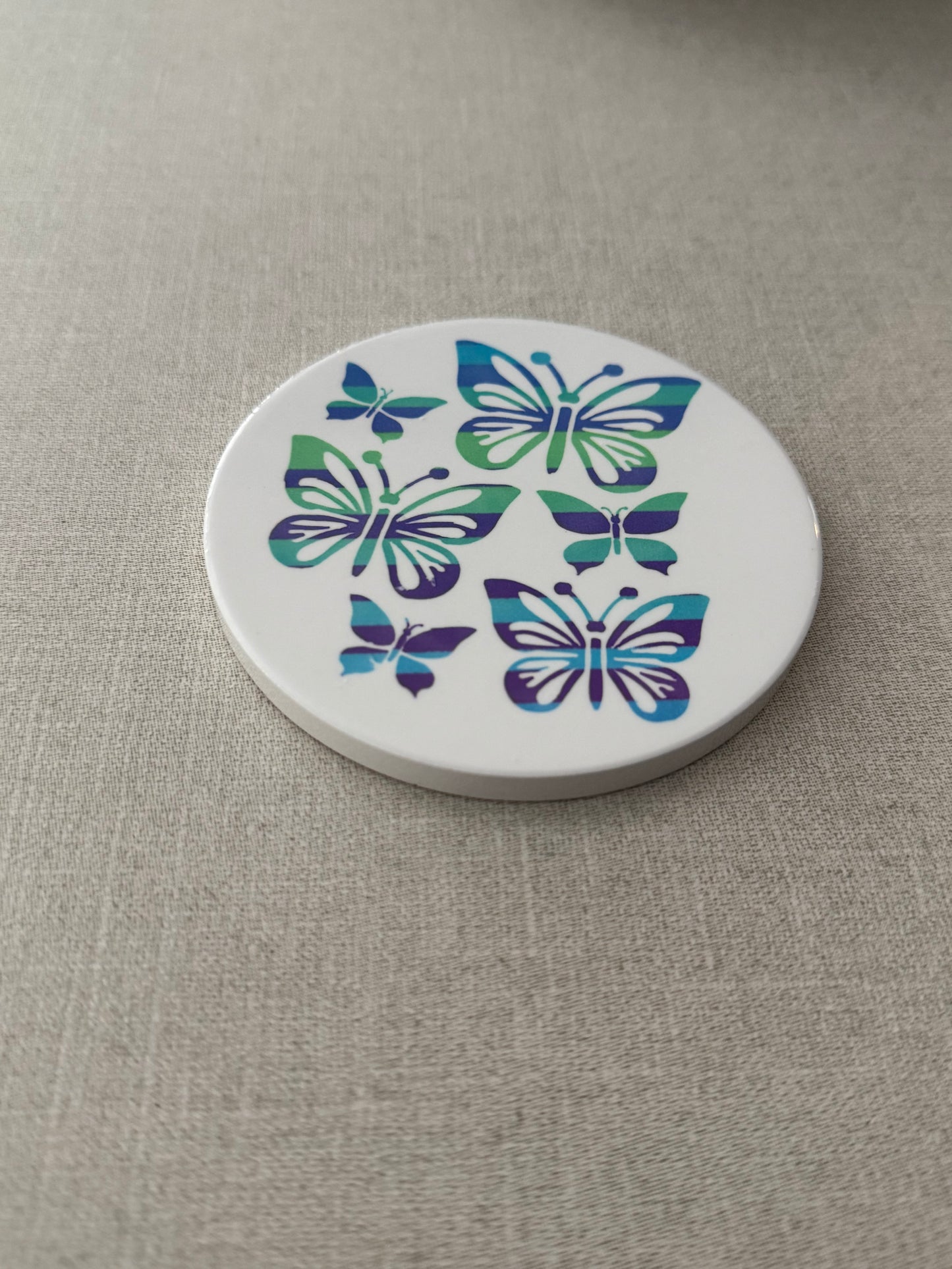 Round ceramic white coaster designed with blue and green butterflies.