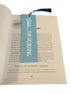 Book with a light blue bookmark labeled 'Shhh... I'm reading' on a textured surface