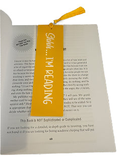 Book with a yellow bookmark labeled 'Shhh... I'm Reading' on a white surface.