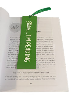 Book with a green bookmark labeled 'Shhh... I'm reading' on a textured surface