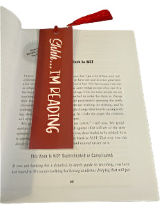 Book with a red bookmark labeled 'Shhh... I'm reading' on a white surface.