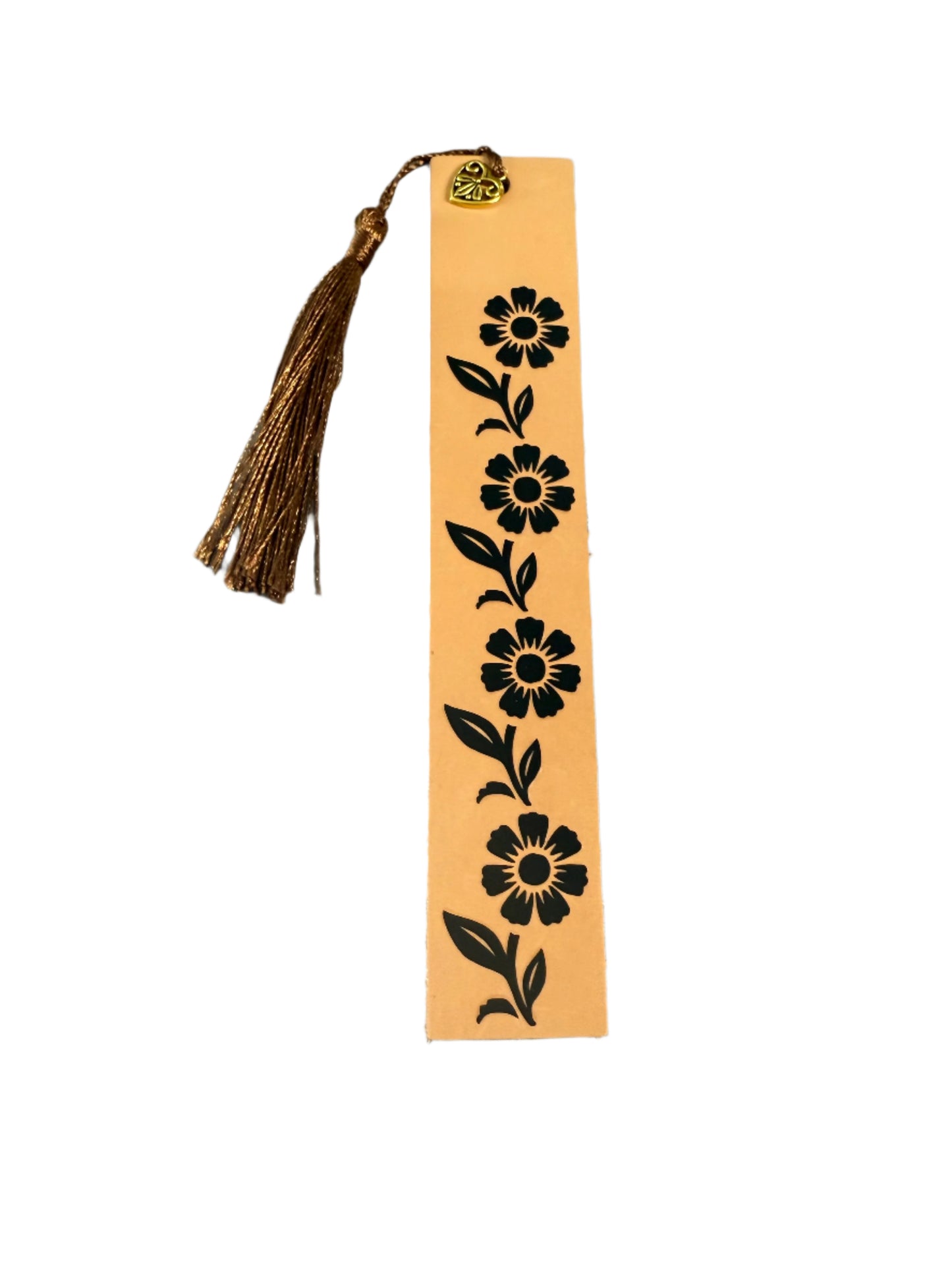 A tan leather bookmark with a black vine pattern, heart charm, and a brown tassel, placed on a neutral background.