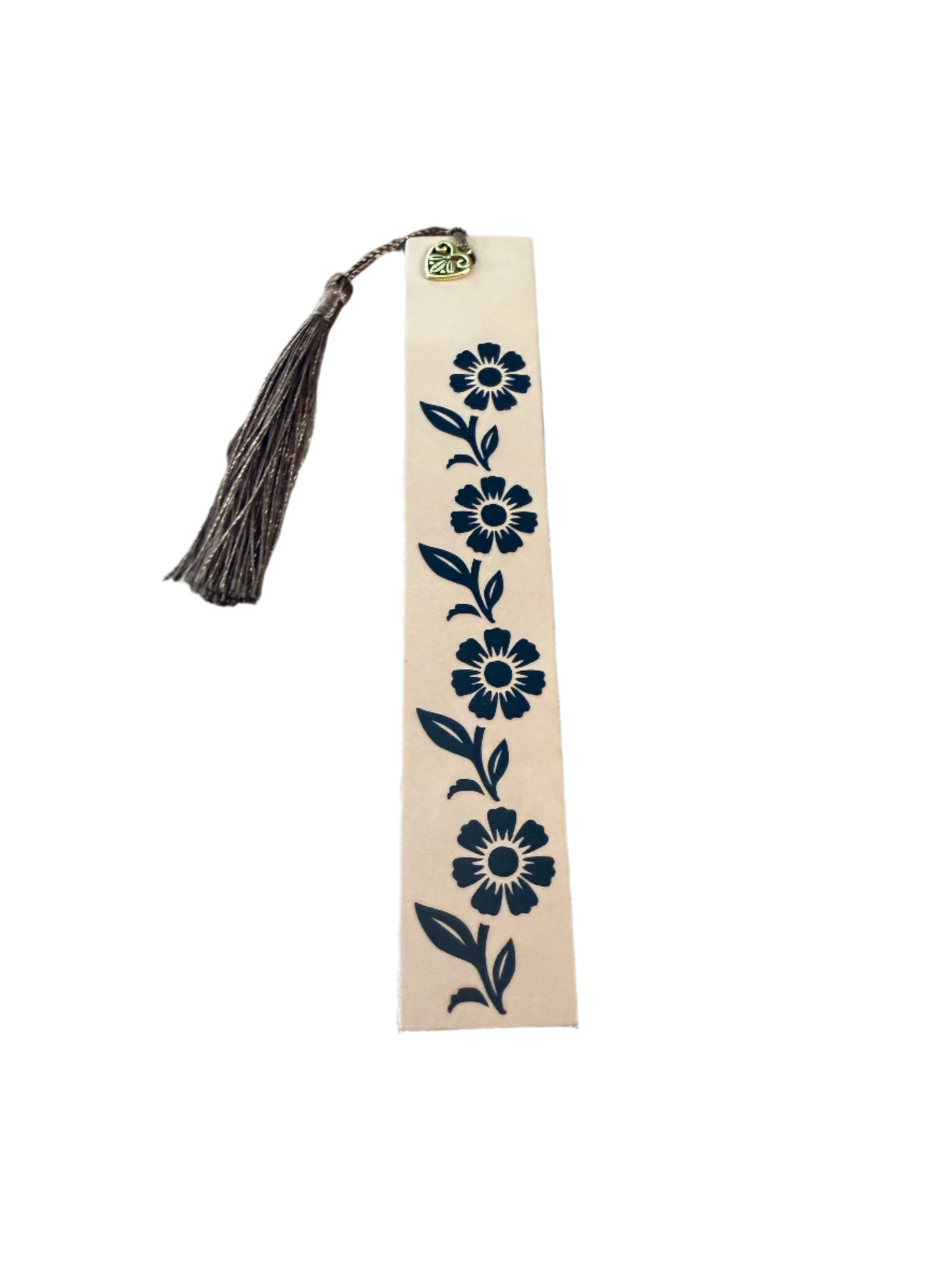 A tan leather bookmark with a black vine pattern, cross charm, and a brown tassel, placed on a neutral background.