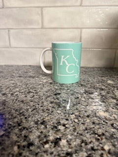 Teal coffee mug with KC design and white handle.