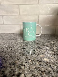 Teal coffee mug with a white KC design on a kitchen counter.