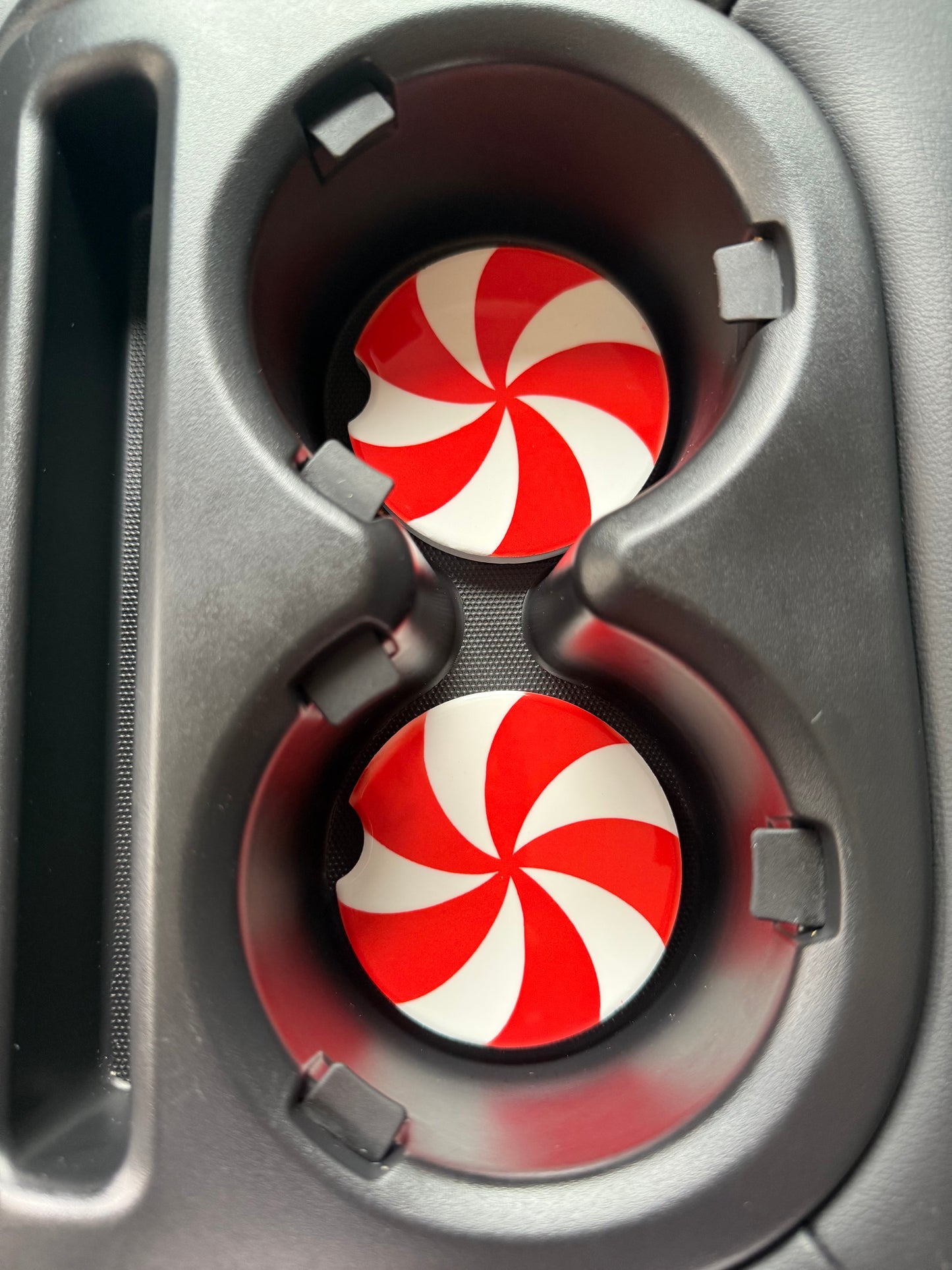 Two red and white peppermint patterned car coasters in a cup holder.