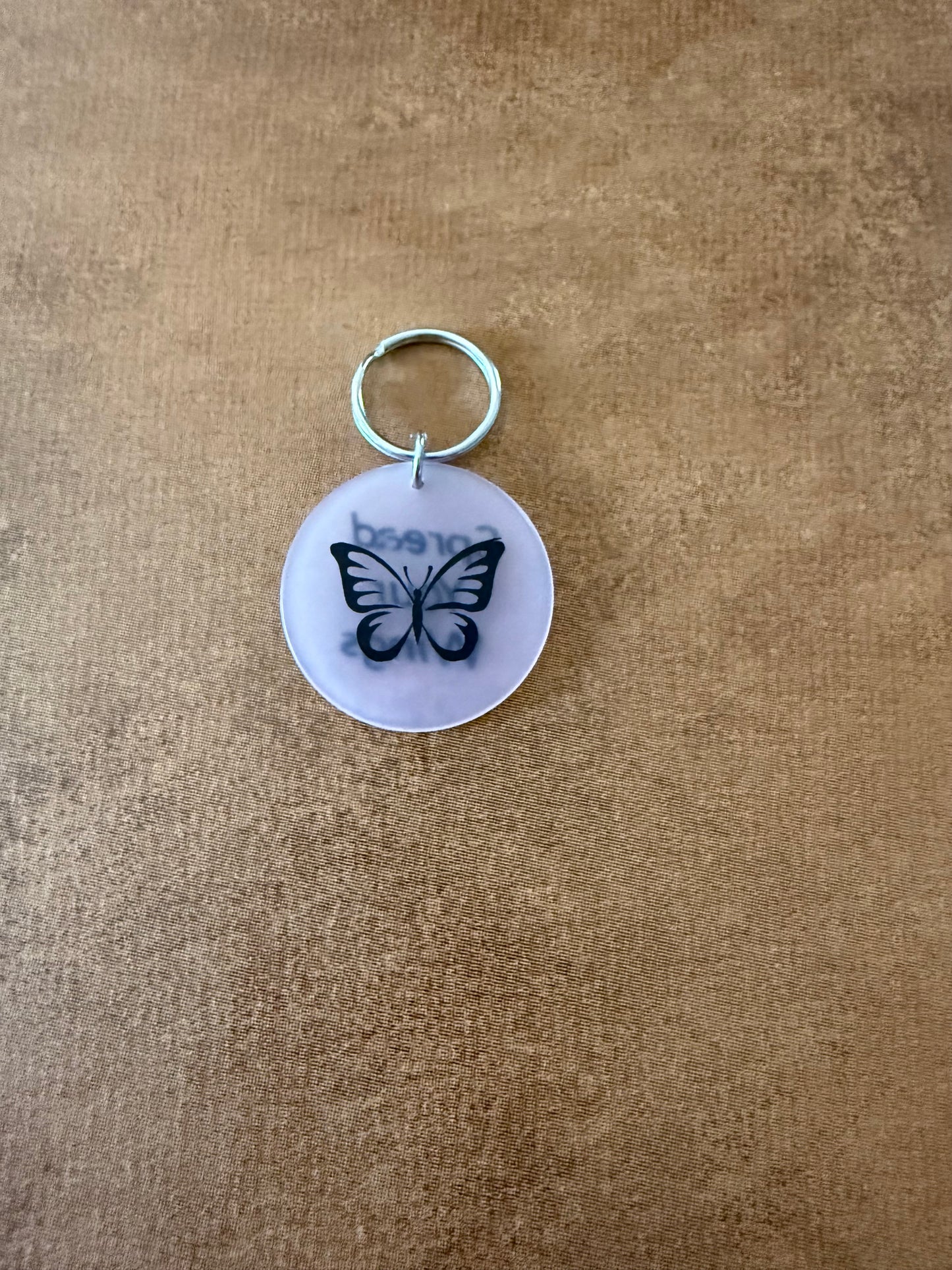 White acrylic butterfly keychain with "Spread Your Wings" on the reverse side.