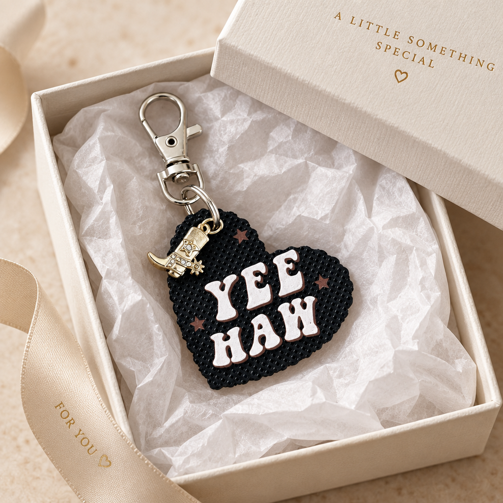 Black heart bag charm with pale pink Yee Haw lettering, brown stars, dangling cowboy boot charm, and silver-tone clasp in a white gift box. Roxzell