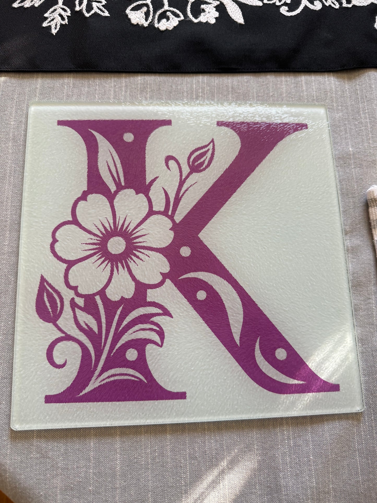 Tempered glass cutting board featuring a stylized purple “K” with floral accents on frosted white, Roxzell
