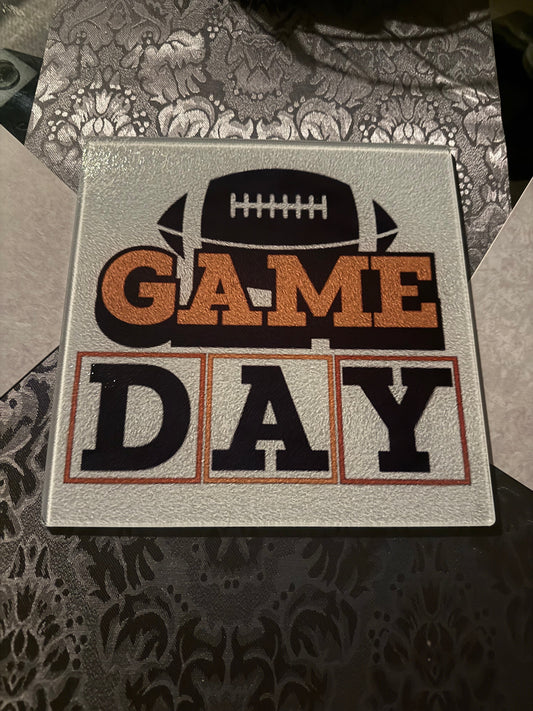 Acrylic glass cutting board with a brown football and orange and brown "Game Day" theme on a table with a gray pattern table runner.