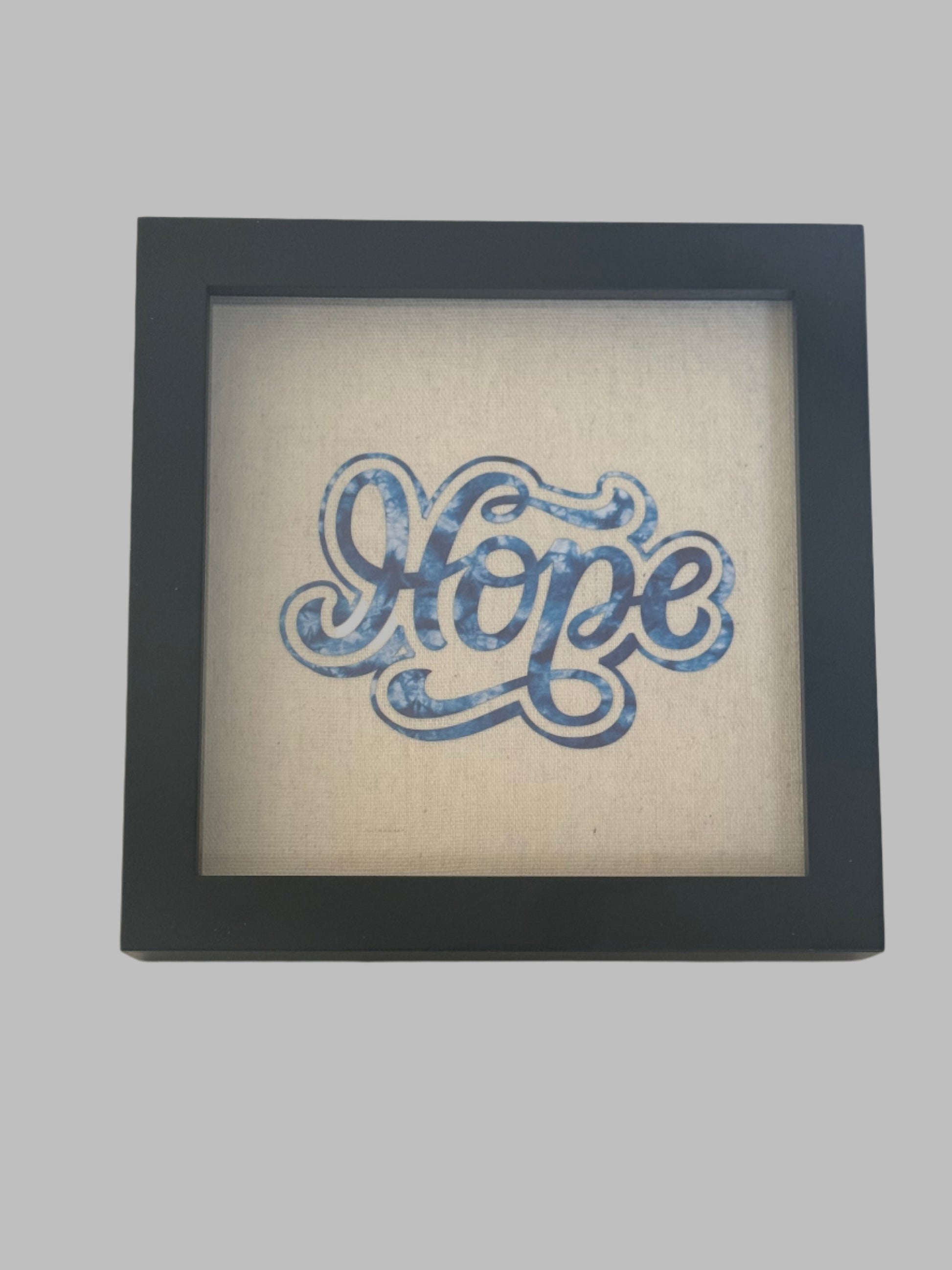 8 x 8 Black frame shadow box designed with the work "Hope" in blue on tan canvas.