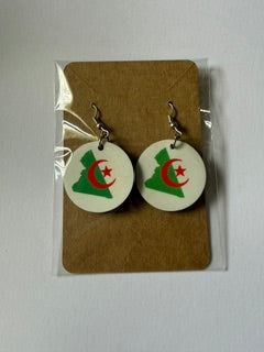 Algeria crescent and star earrings attached to a brown backing card inside a clear plastic sleeve, showing green map shapes with red crescent and star design. Roxzell