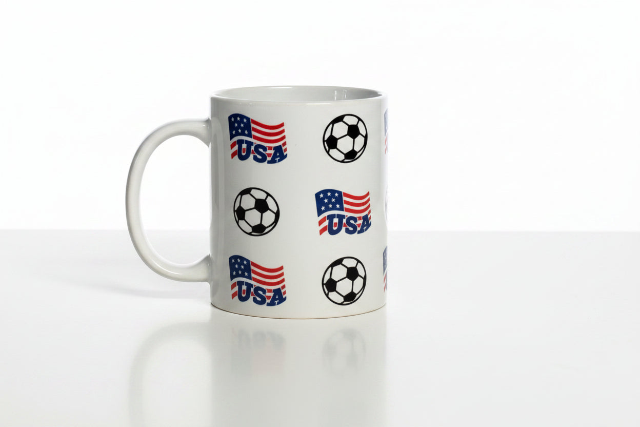 Glossy white mug decorated with stylized American flags labeled “USA” and soccer balls, celebrating national football pride.