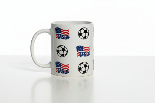 Glossy white mug decorated with stylized American flags labeled “USA” and soccer balls, celebrating national football pride.