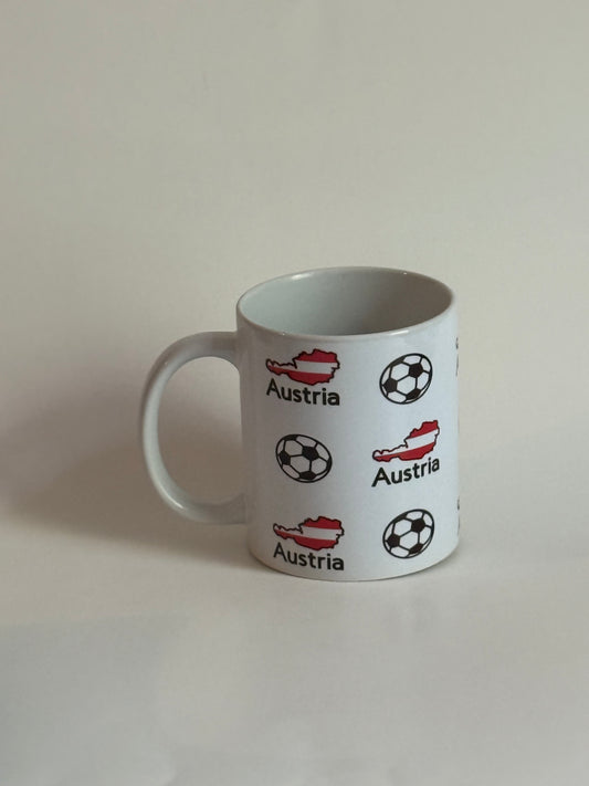 White ceramic mug featuring Austria’s red‑and‑white map outline and black‑and‑white soccer ball pattern, symbolizing national football pride.