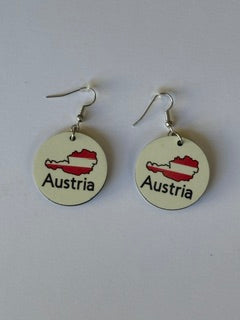 Pair of circular earrings featuring Austria’s map outline filled with red and white flag colors and the word “Austria” printed below, displayed on a white surface. Roxzell
