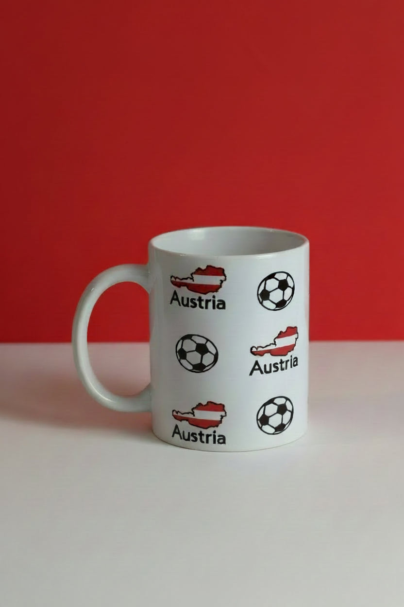 Ceramic mug printed with Austria map silhouettes and soccer balls, on a red and white background, representing Austria’s love for the beautiful game.