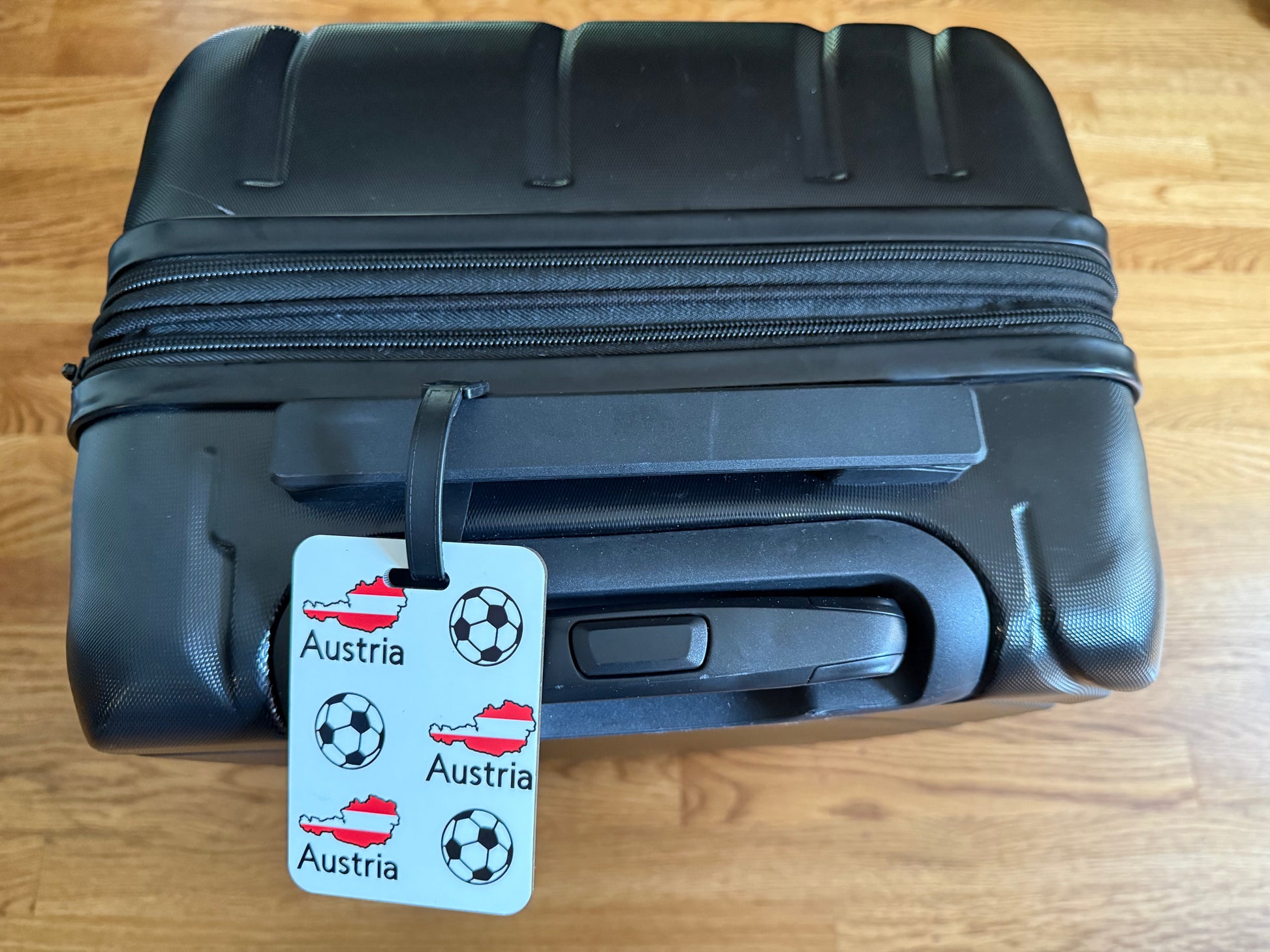 Austrian flag‑inspired travel tag featuring football icons on a black suitcase. Roxzell