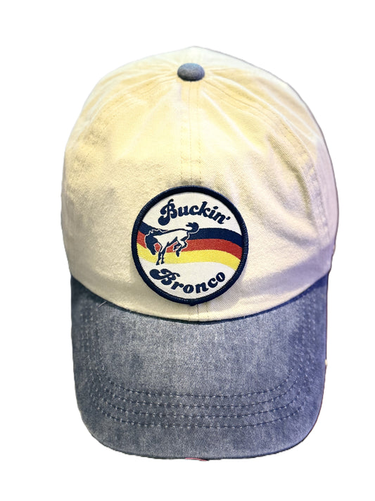 Front view of a beige and denim-blue baseball cap featuring a circular patch with a bucking horse and the text “Buckin’ Bronco” over red, yellow, and blue stripes. Roxzell