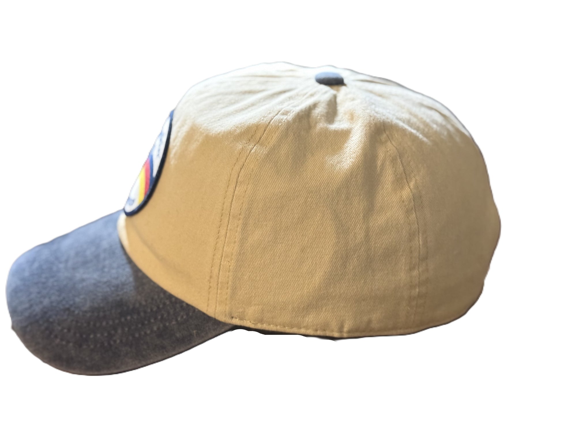 Left side view of a beige and denim-blue baseball cap featuring a circular patch with a bucking horse and the text “Buckin’ Bronco” over red, yellow, and blue stripes. Roxzell