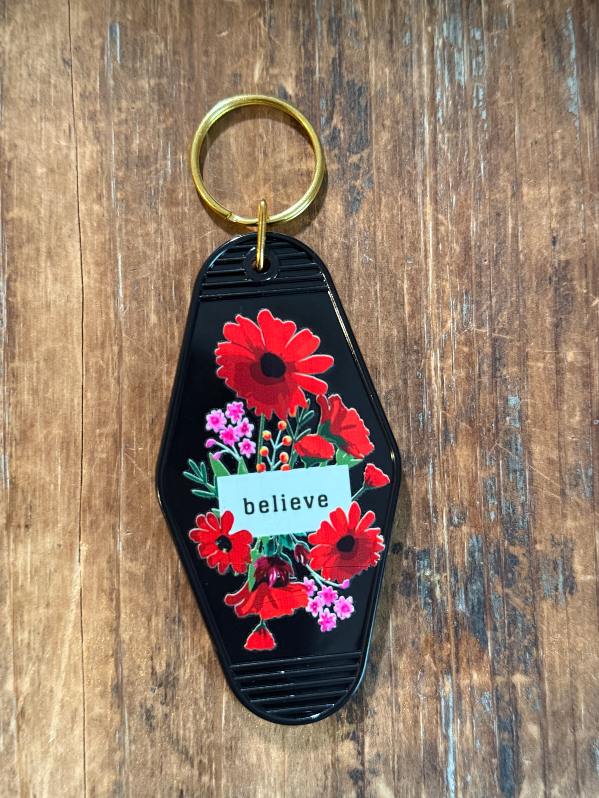 Black Believe motel-style keychain with red floral artwork. Roxzell