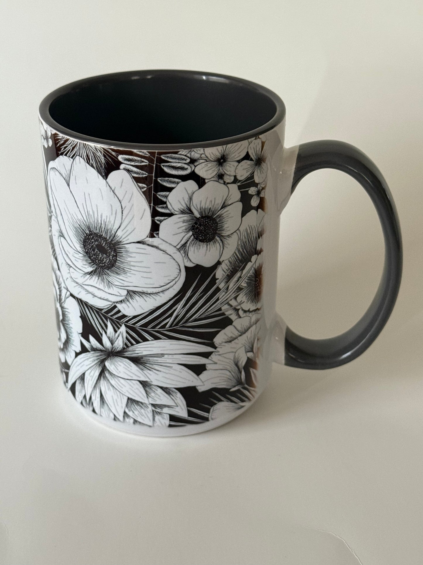 A ceramic mug with intricate white botanical flowers on a glossy black background, resting on a white surface. Roxzell