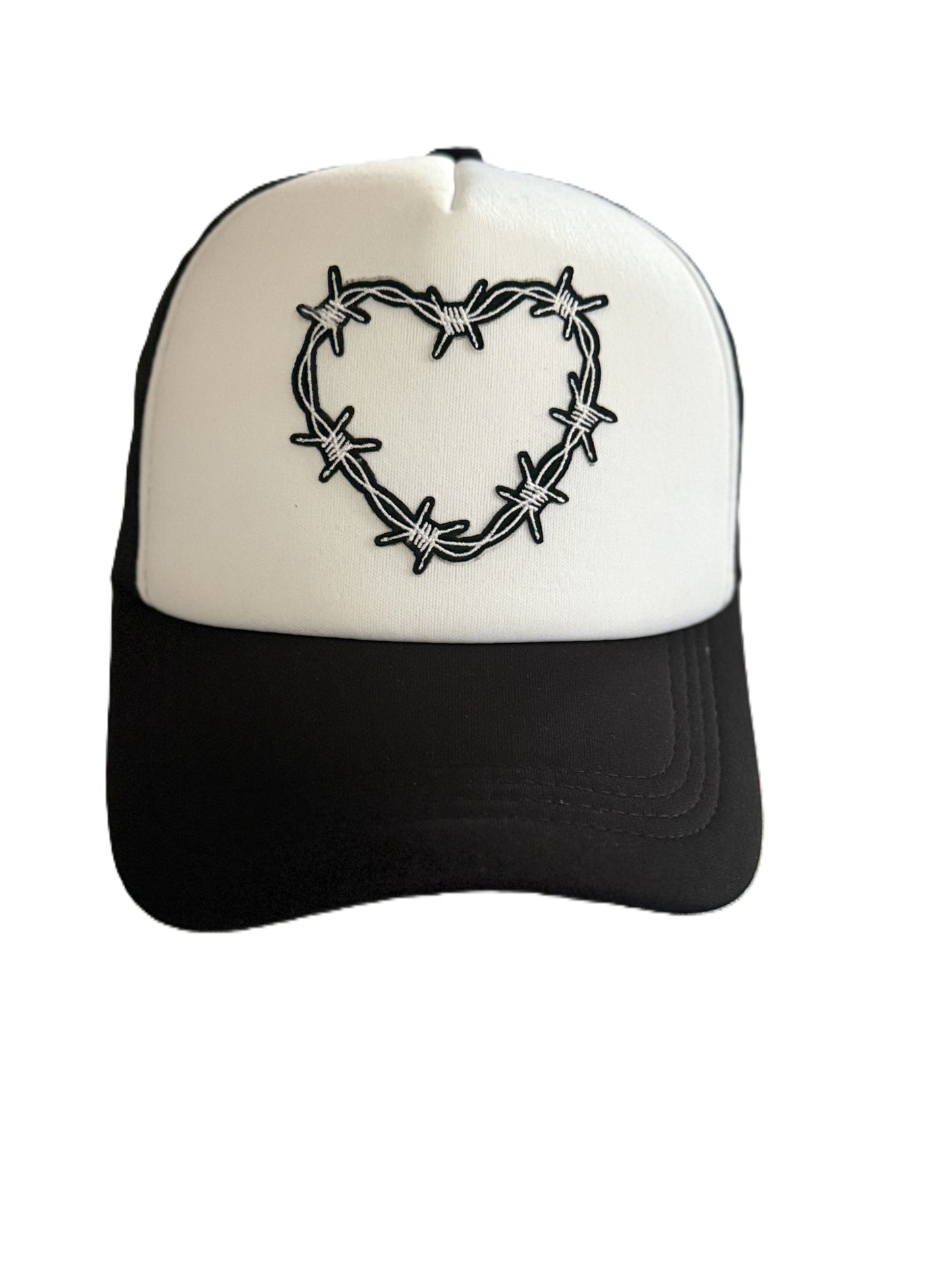 Front view of a trucker hat featuring a white front panel with a black barbed‑wire heart design patch and a black brim. Roxzell