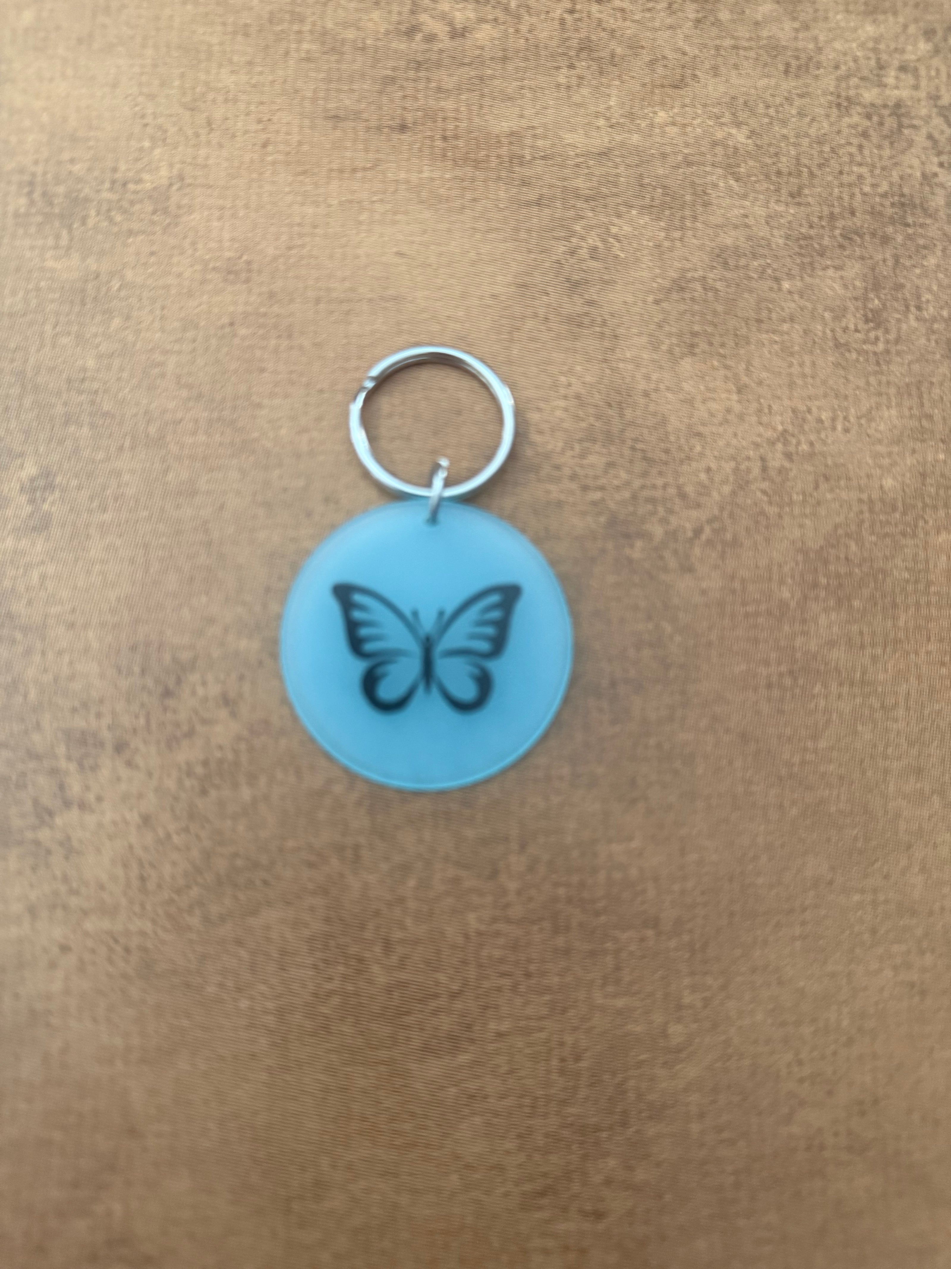Blue acrylic butterfly keychain with "Spread Your Wings" on the reverse side.