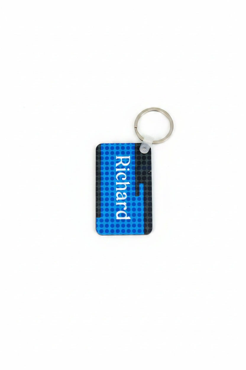 Blue rectangular keychain with a dotted pattern and the name “Richard” printed in white, attached to a silver ring on a rustic wooden surface.