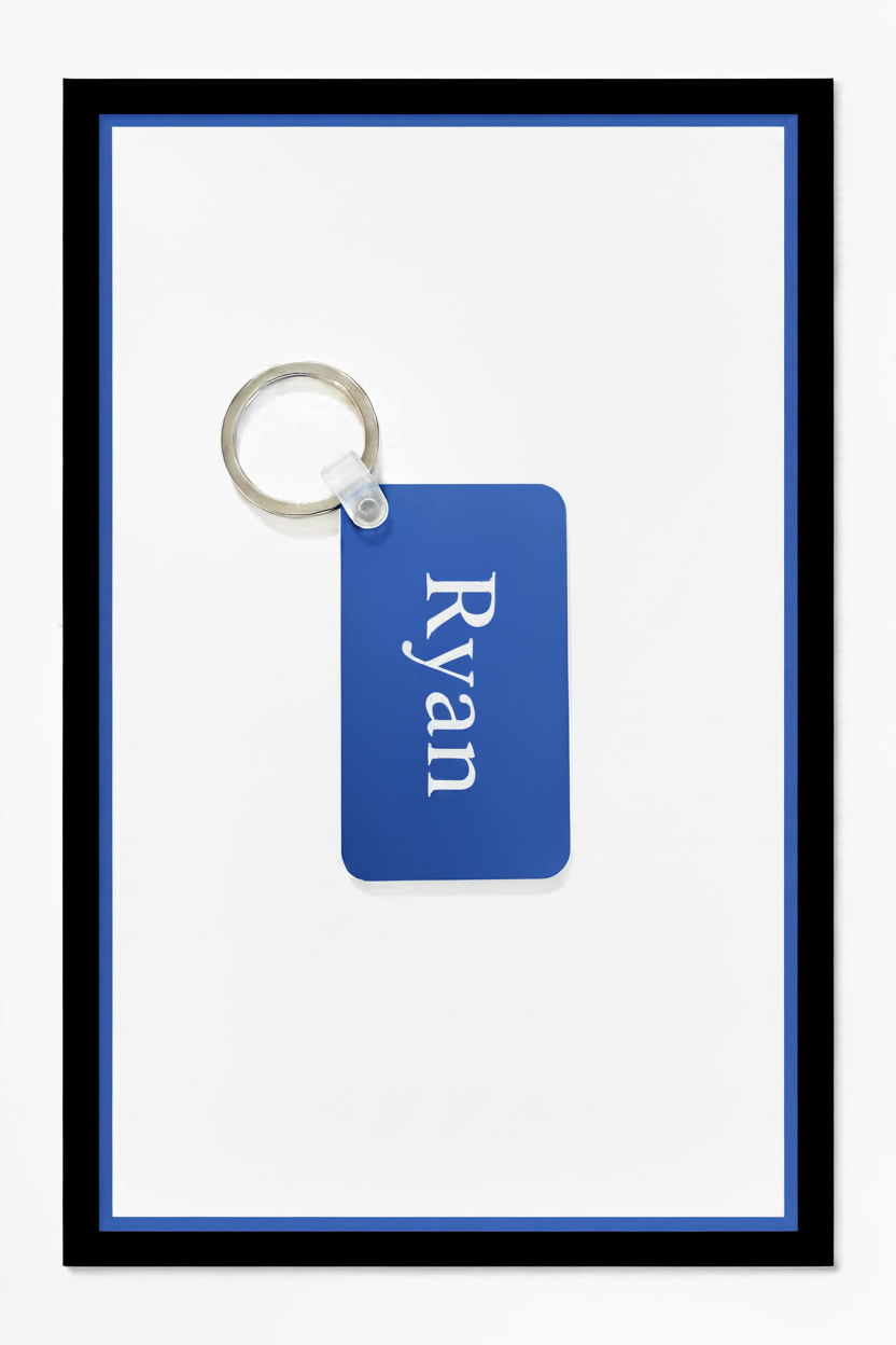 A personalized blue rectangular keychain tag with the name 'Ryan' printed in white serif text, attached to a silver metal key ring, set against a white background with a blue inner border and black outer frame. Roxzell