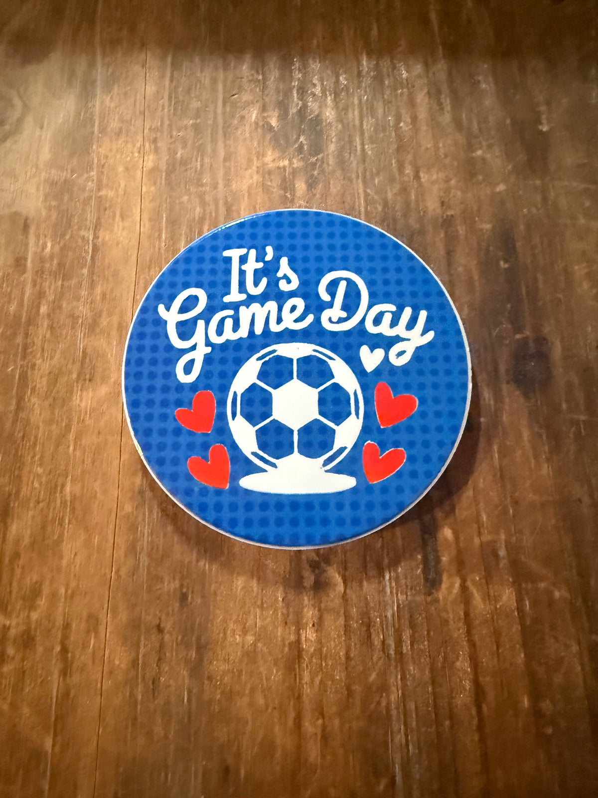 Round blue coaster featuring white “It’s Game Day” text, soccer ball, and red heart details. Roxzell
