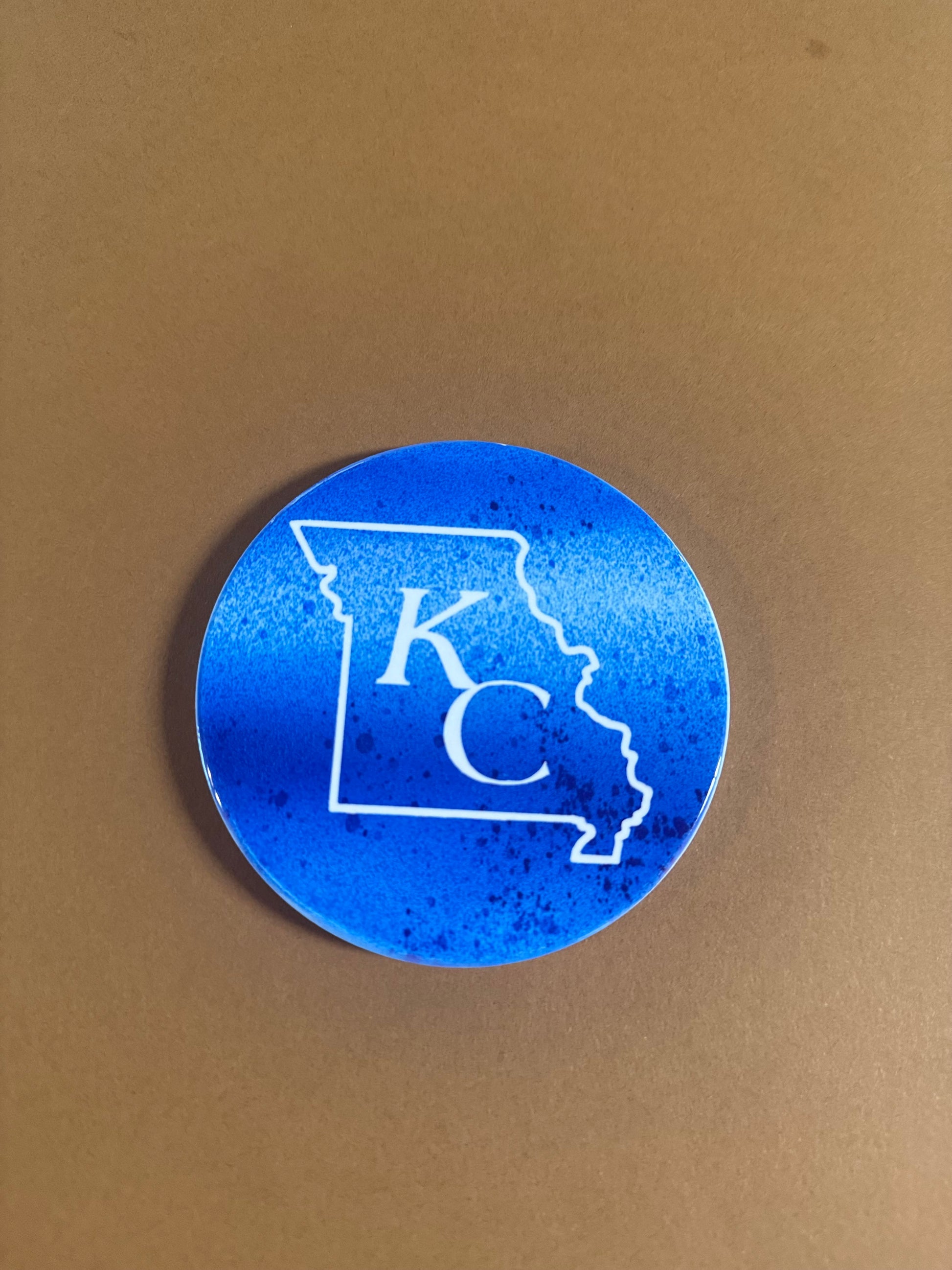 Blue and white round ceramic coaster with KC designed inside the shape of Missouri.