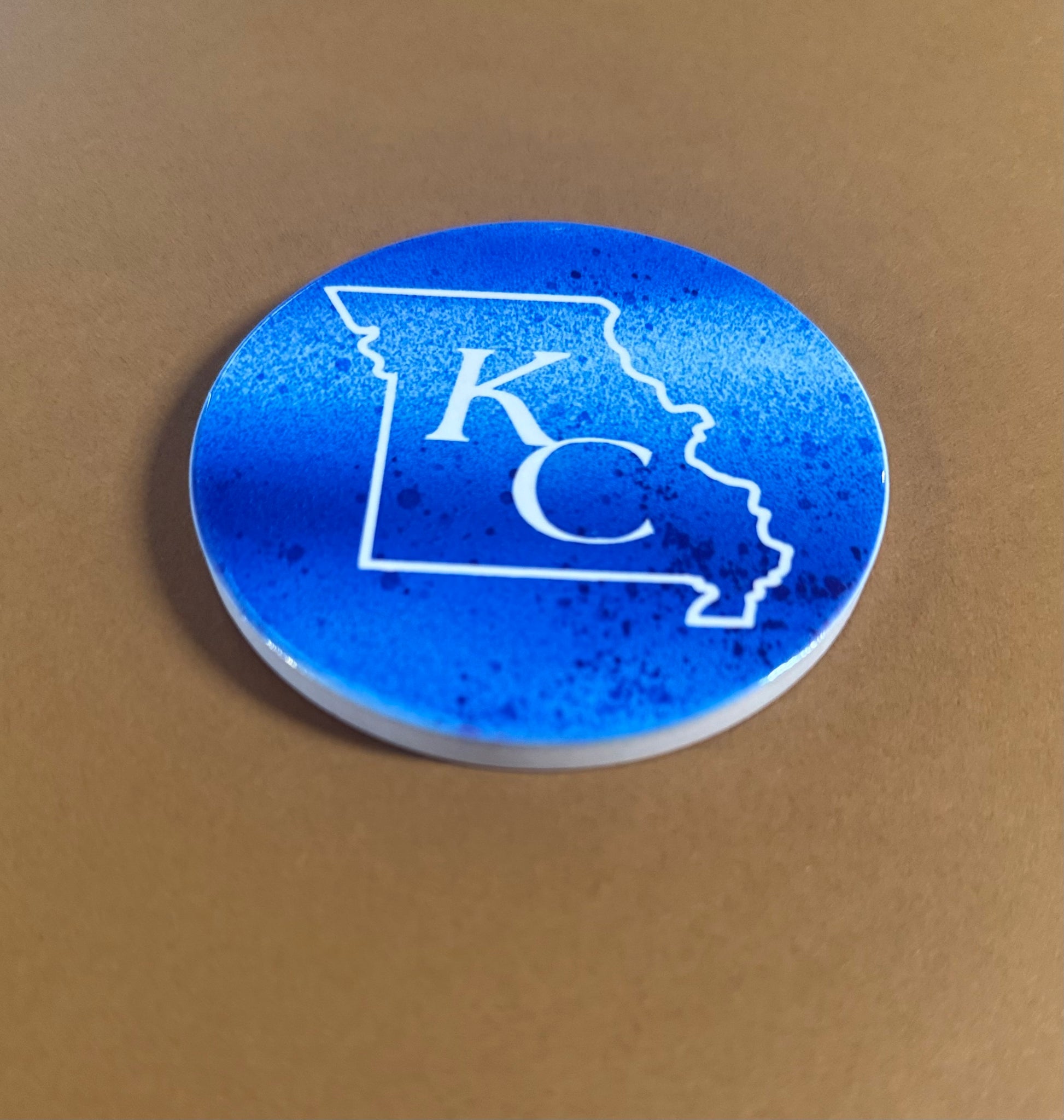 Blue and white round ceramic coaster with KC designed inside the shape of Missouri.